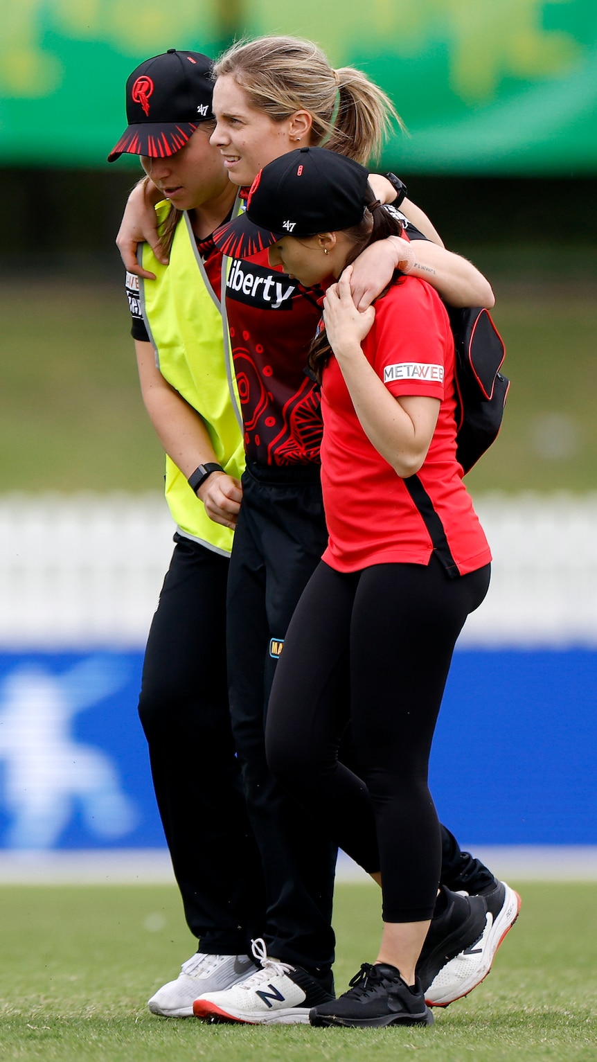 A cricketer is helped off the field by teammates after suffering a serious knee injury