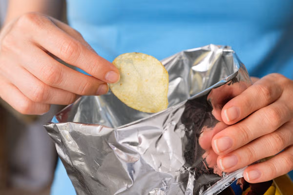 The girl takes crispy fried fatty potato chips from a package or pack. 