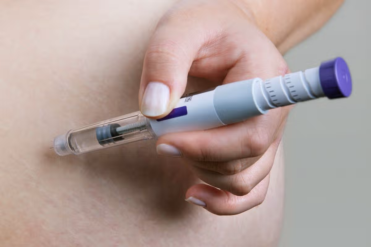 Weight loss drug and diabetes treatment. Close-up of person using portable Mounjaro insulin injector pen or GLP-1 injection for subcutaneous shot in abdomen. Obesity therapy, hormonal medication, semaglutide injection, modern healthcare lifestyle