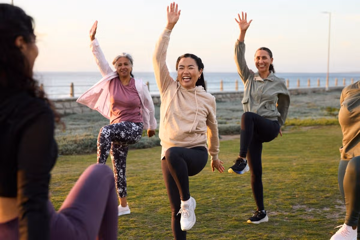 Happy mature woman exercising with friends. Active females are following fitness instructor. They are enjoying in garden at morning.