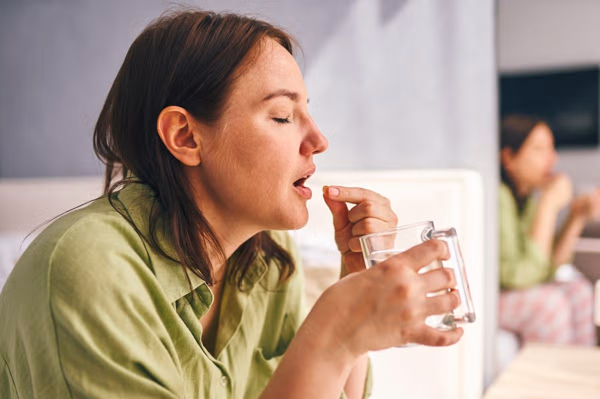 Adult woman taking a pill with water