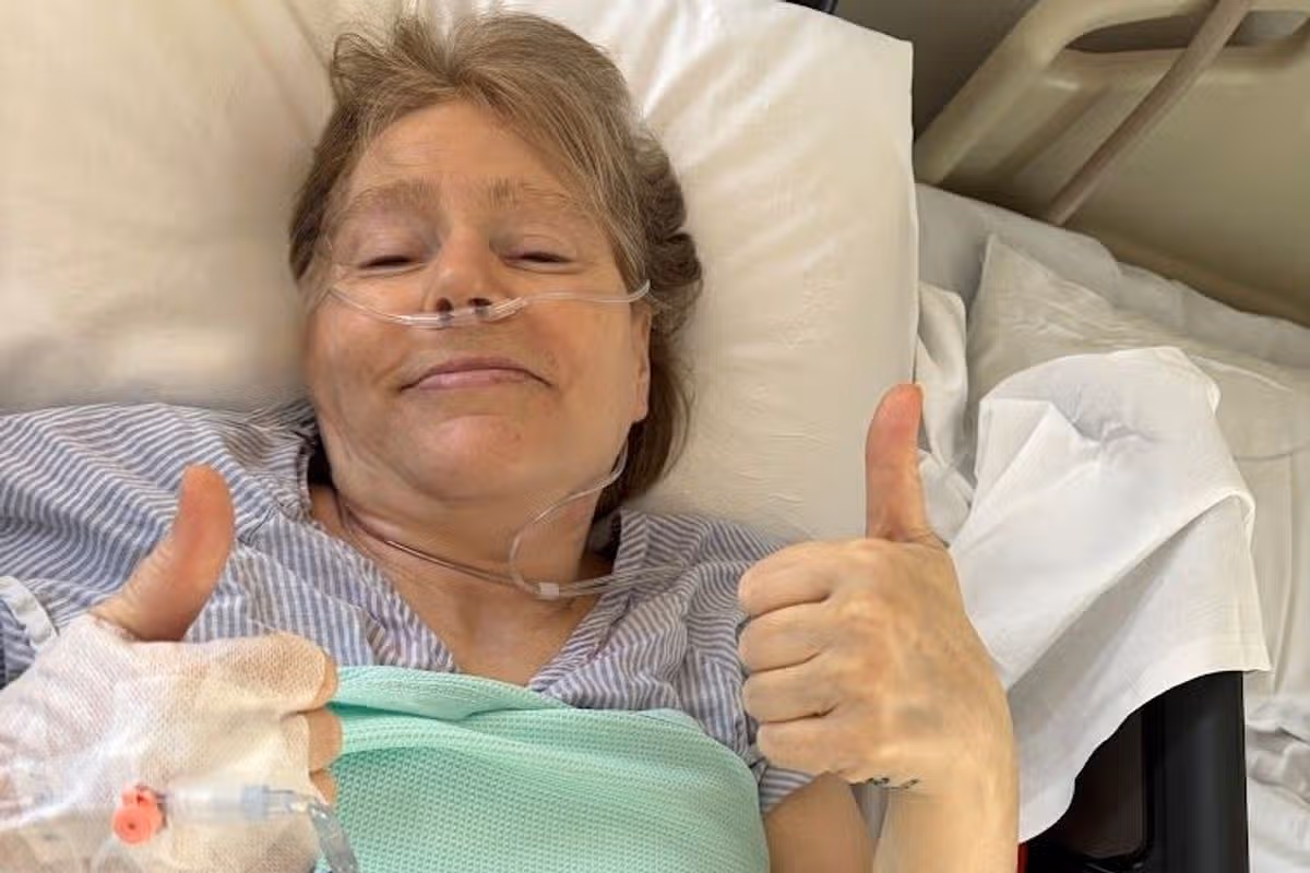 A woman lying in a hospital bed giving the thumbs up