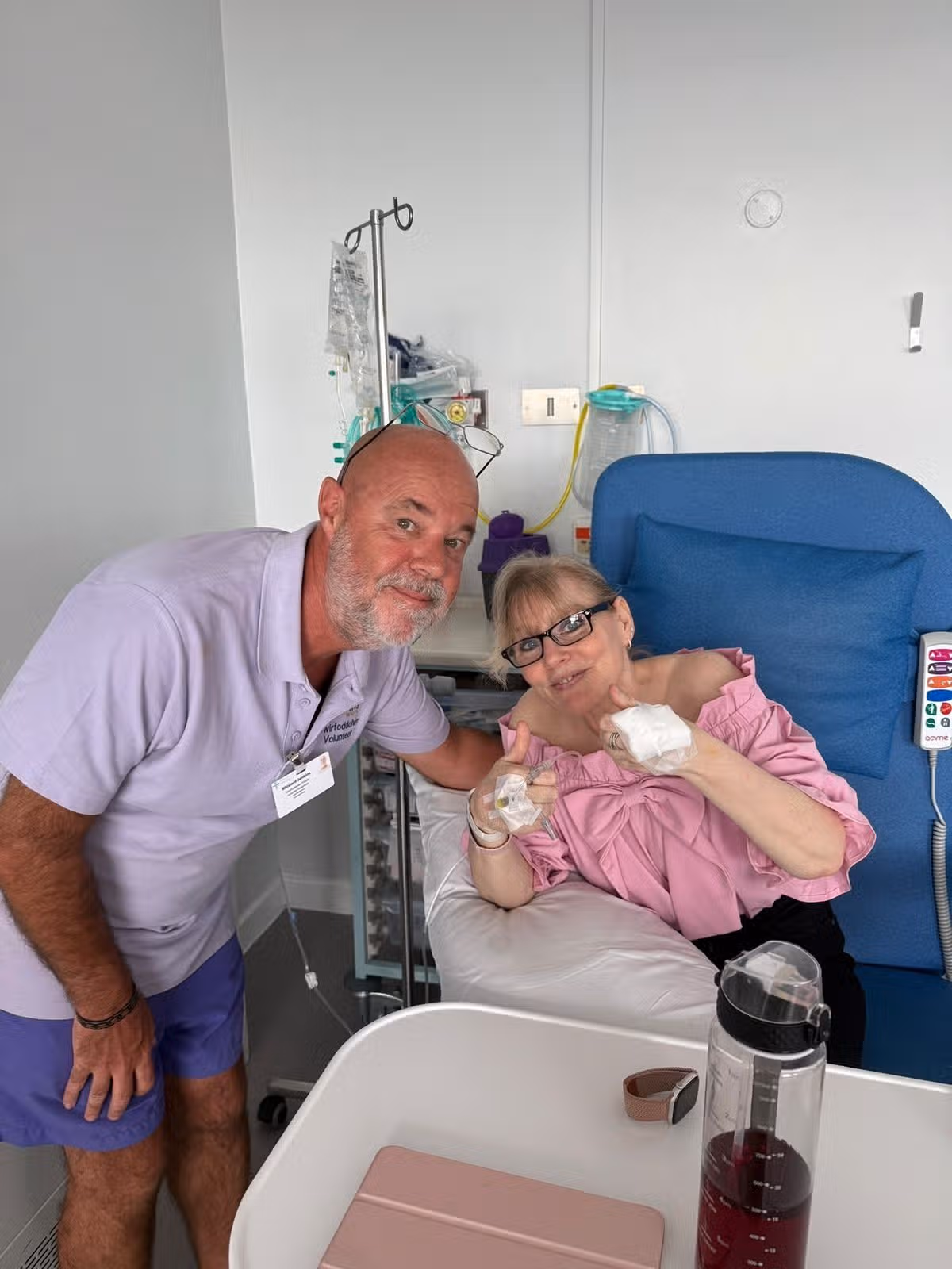 A woman sat in a chair in a hospital with a man stood next to her