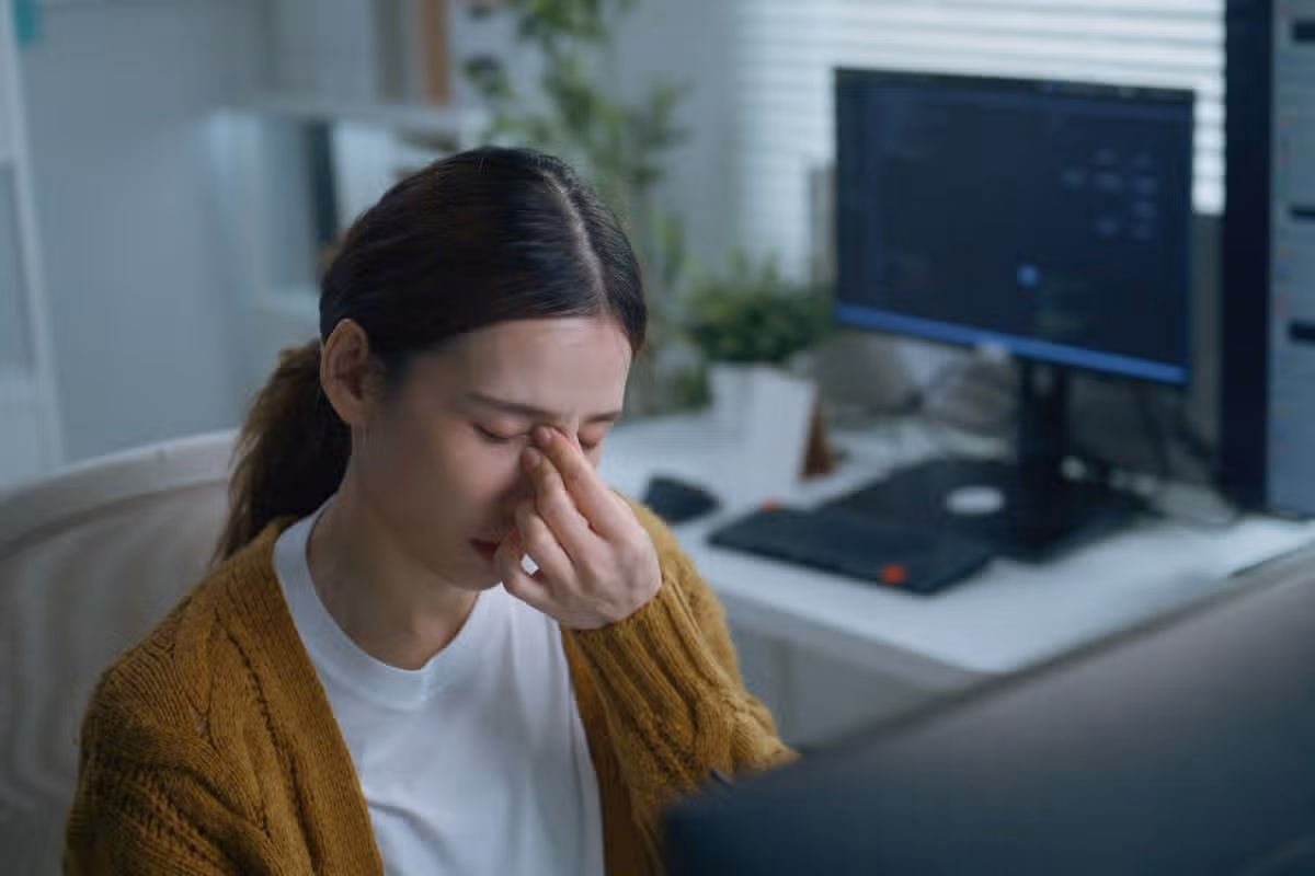 Office worker experiencing eye strain and tired eyes while working at a computer, illustrating digital eye fatigue, screen time, workplace health, discomfort, stress, and desk job.