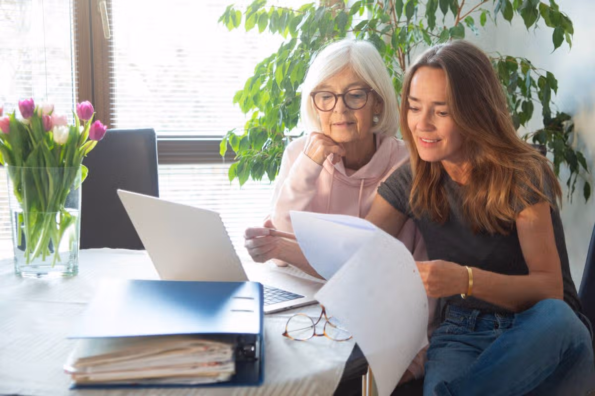 Senior woman and her daughter going through paperwork, using laptop computer