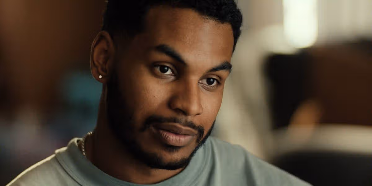 An individual wearing a gray t-shirt, with a close-up view of the face, showcasing a slight smile and a glimpse of a blurred background.
