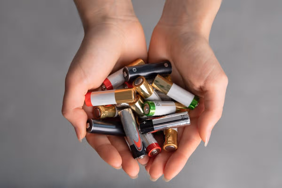top view view of hands full of alkaline batteries, hands of young caucasian girl, white sweater in background, disposal of chemical current sources