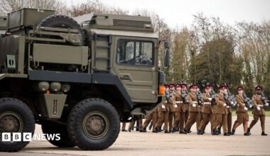 Troops march eyes right next to an Army vehicle.
