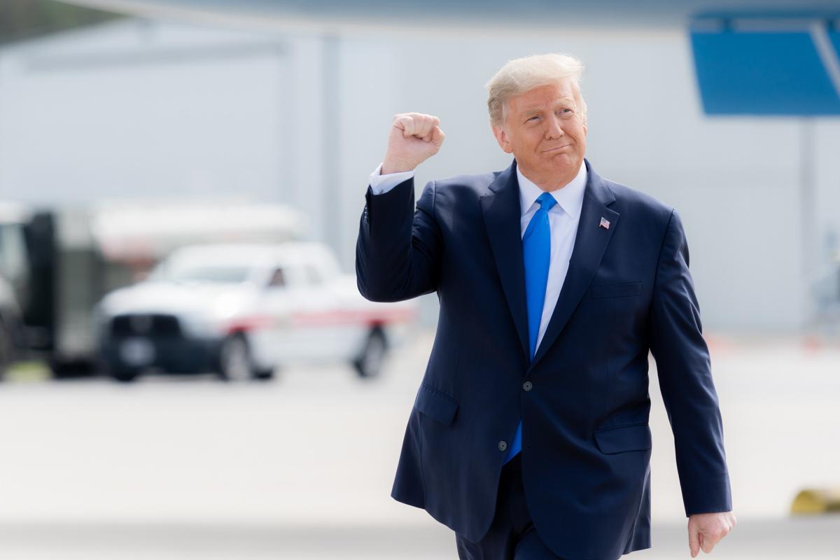 Donald Trump is raising his right hand in a fist while walking across an airport tarmac. 