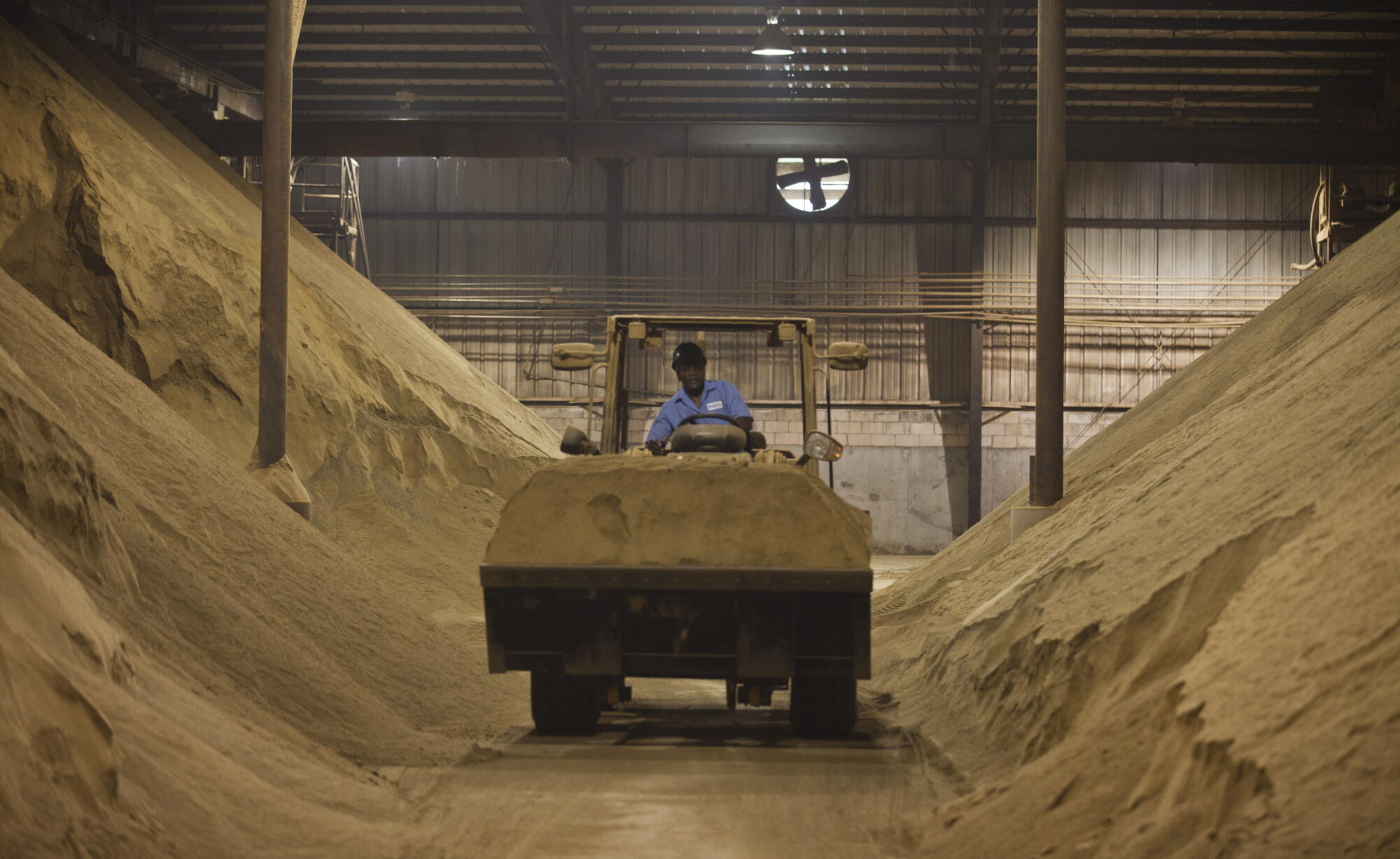 A worker drives a tractor past mounds of dried and crushed Menhaden fish