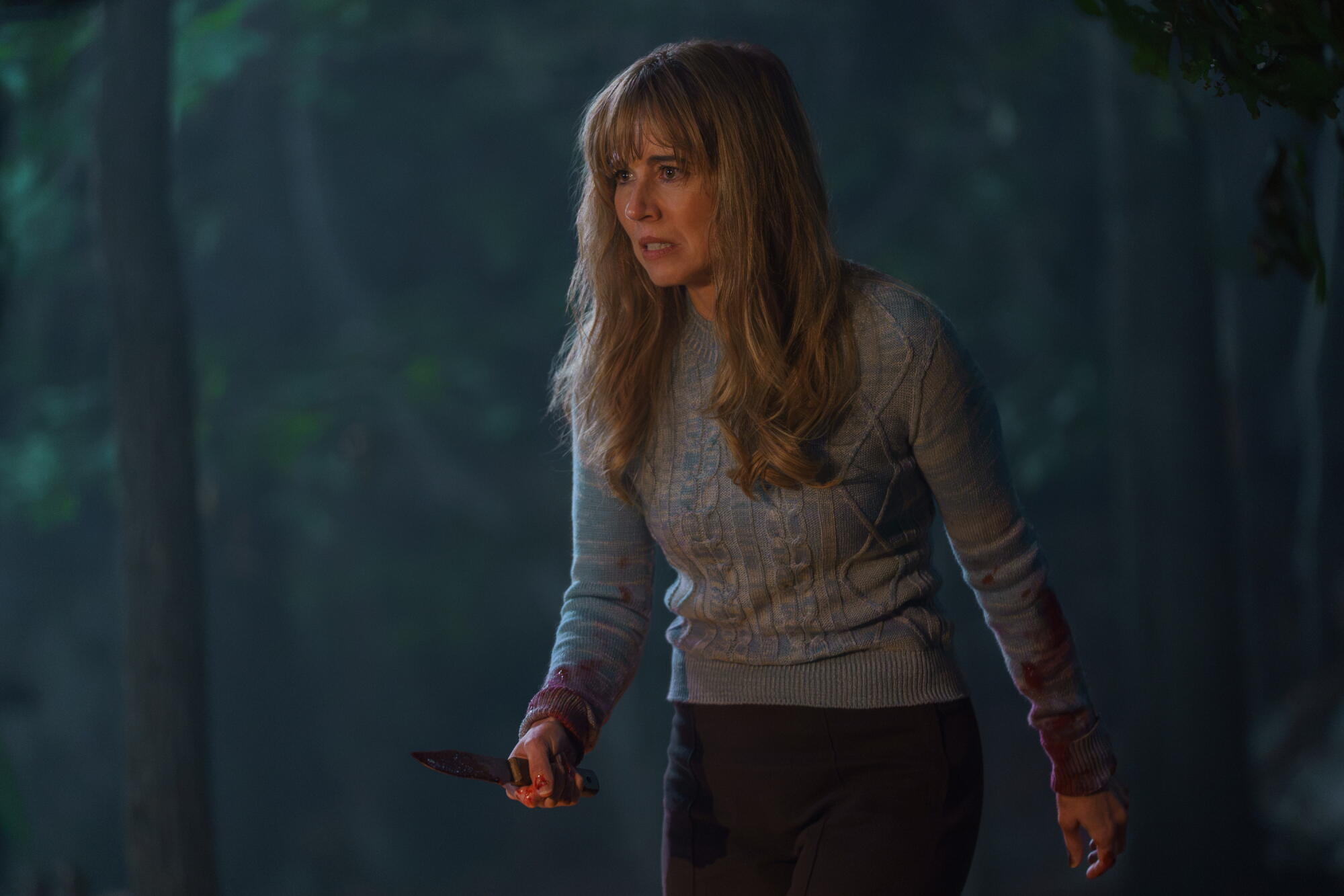 A woman in a blue sweater holding a knife in one hand.