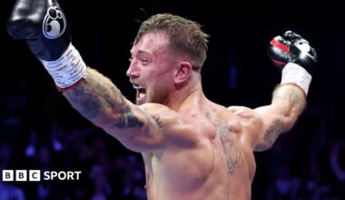 Brad Pauls stands with his back to the camera and his arms held in the air in celebration. He is wearing boxing gloves and his mouth is open