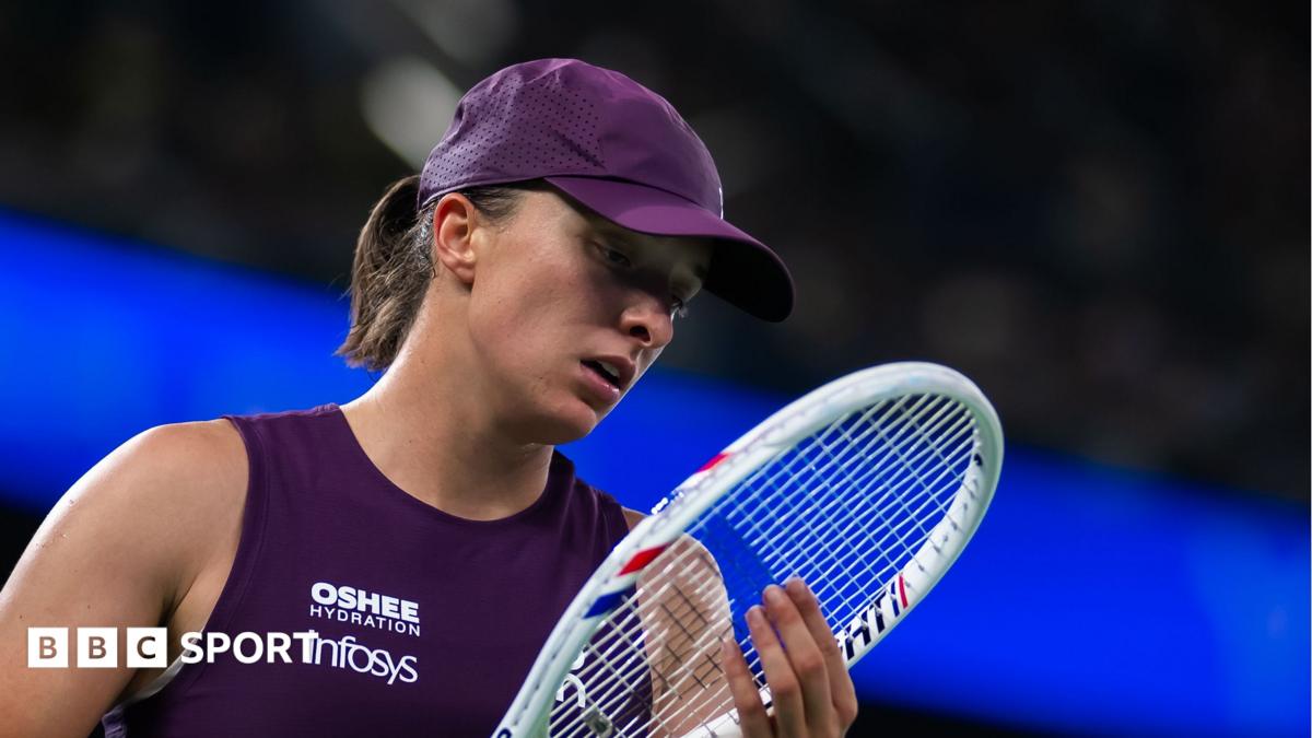 Iga Swiatek, in purple sleeveless tennis top and purple cap, looks at her racquet during a Wuhan Open semi-final defeat
