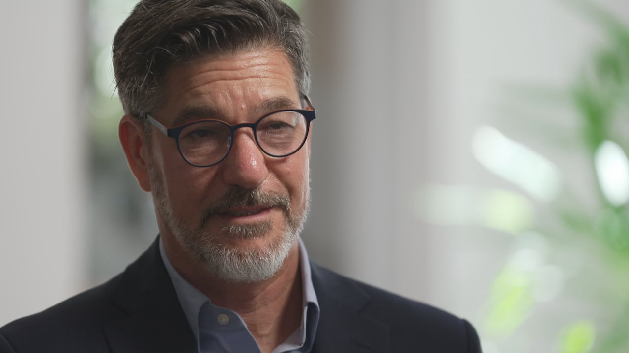 A close up photo of a man with beard, dark framed glasses, suit.