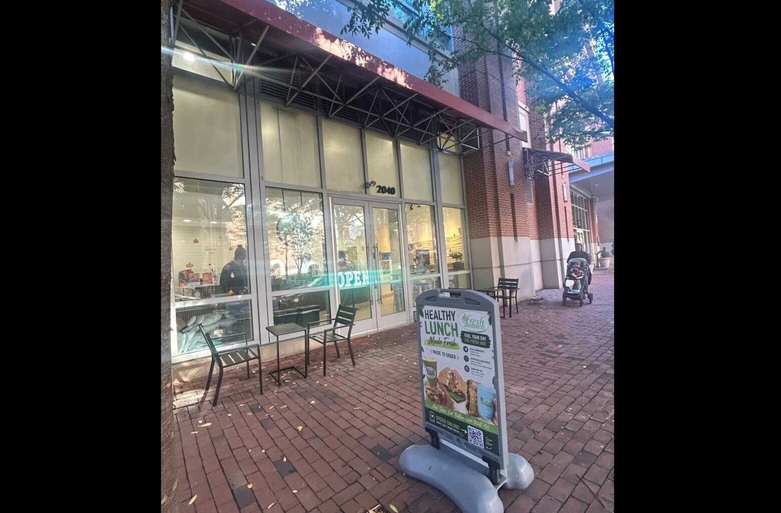 Cafe storefront with large glass doors, red awning, and outdoor tables on a brick sidewalk; a menu sign outside.