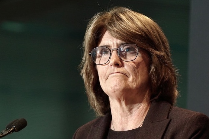 Michele Bullock looks like she is frowning. A small black microphone is in the lower left corner of the photo.