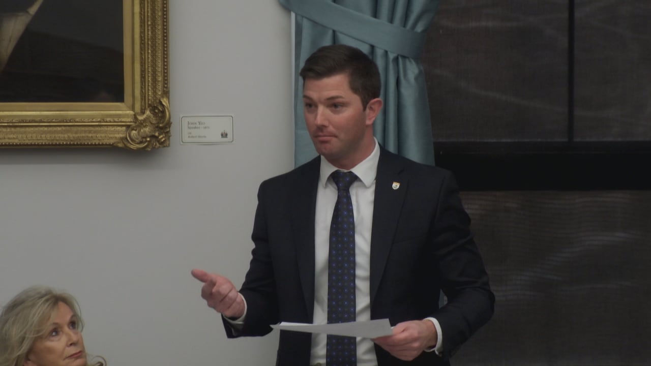 A man in a dark suit and white shirt responding to questions in the P.E.I. Legislature.