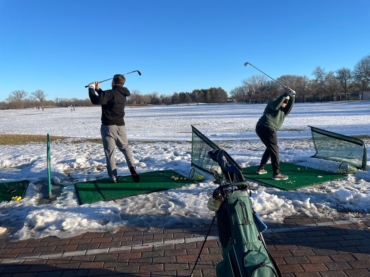 People swinging golf clubs in a snowy field.
