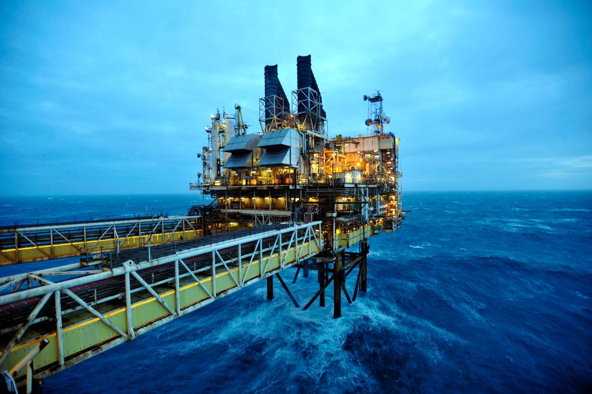 Offshore oil rig platform with illuminated facilities and a long gangway over choppy North Sea waters.