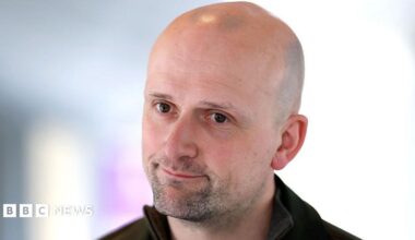 Stephen Flynn looking slightly off camera. Only his head and shoulders are visible and he appears to be wearing a dark top.