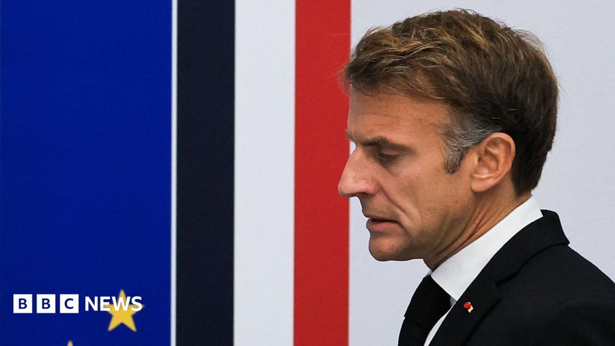 Close up of French President Emmanuel Macron taken from the side. He has short brown hair, and is wearing a white shirt, black jacket and tie.