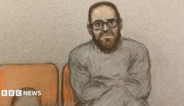 A court sketch of Joshua Kerry. He sits with his legs and arms crossed on an orange chair. He is wearing glasses and a grey tracksuit.