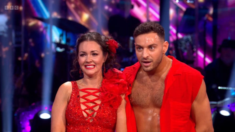 strictly come dancing lacey turner vito coppola two dancers in red costumes on stage with colorful lights in background.