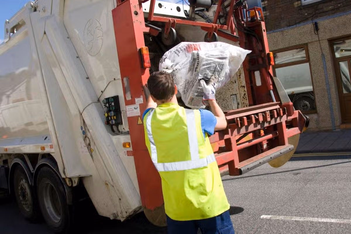 A bin man putting a recycling bag into a bin lorry