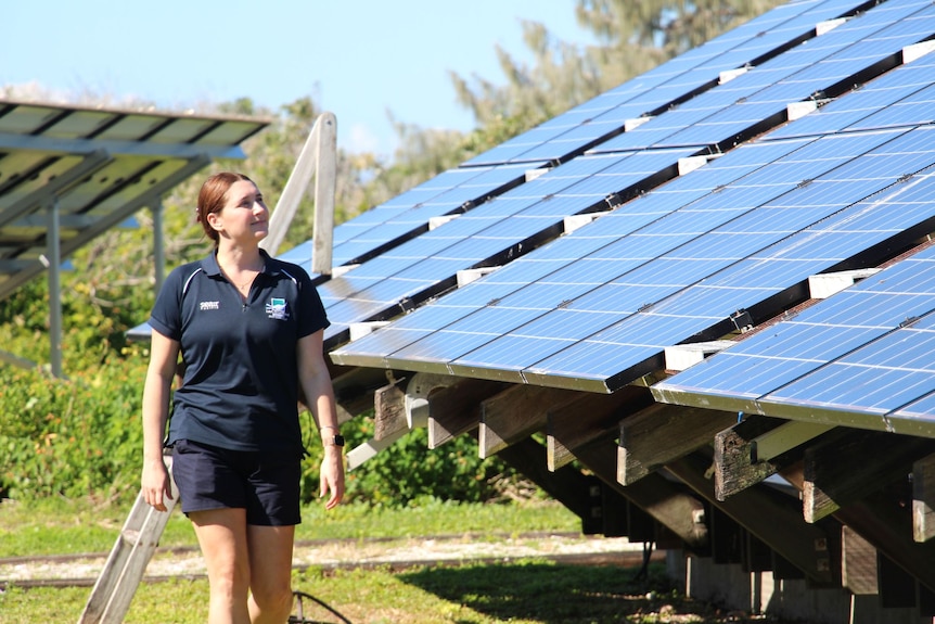 A young woman walks beside lots of solar panels.