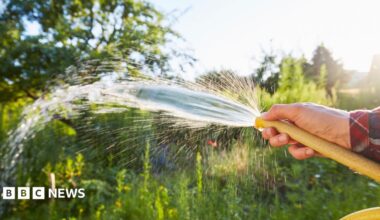 A hosepipe being sprayed with a person's finger in front of its end.