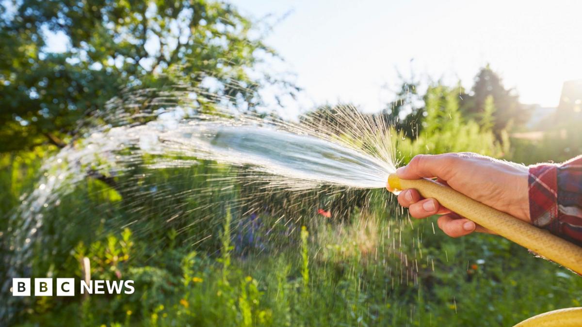A hosepipe being sprayed with a person's finger in front of its end.