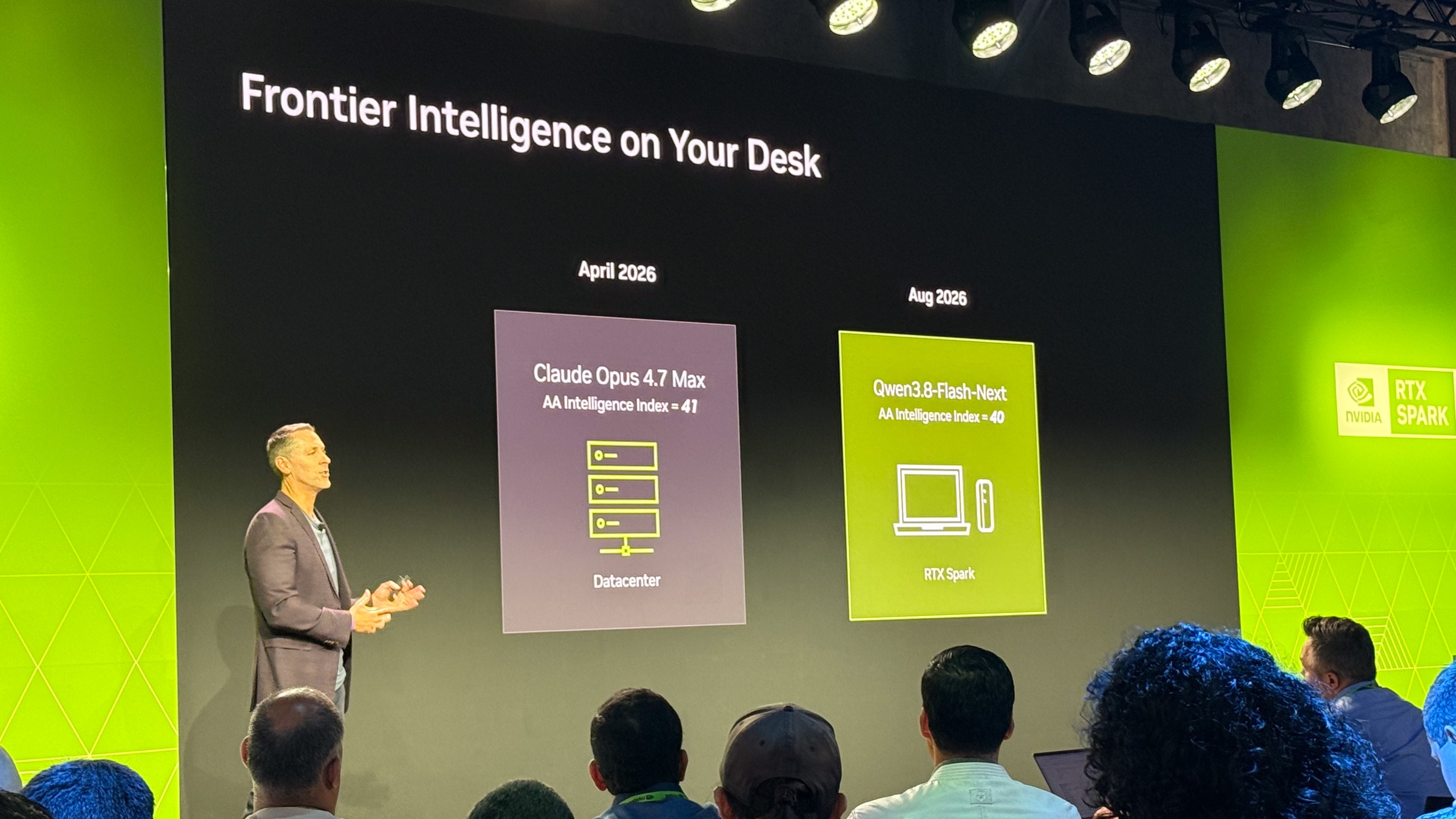 A man presenting on stage, with a slide reading 'Frontier Intelligence on your Desk'. It shows how local models in August 2026 were achieving similar compute as frontier models were in April 2026.