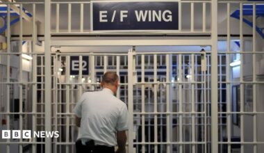A prison guard locks the entrance to a prison wing which says E/F Wing above it.