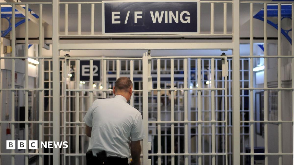 A prison guard locks the entrance to a prison wing which says E/F Wing above it.
