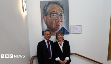 Mr Gerald Gui and artist and former patient Ruth Swain smiling for a photo under his portrait at the Royal Marsden Hospital. They are in the staircase.