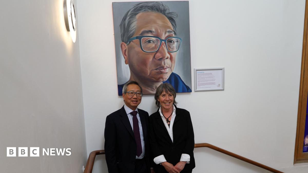 Mr Gerald Gui and artist and former patient Ruth Swain smiling for a photo under his portrait at the Royal Marsden Hospital. They are in the staircase.