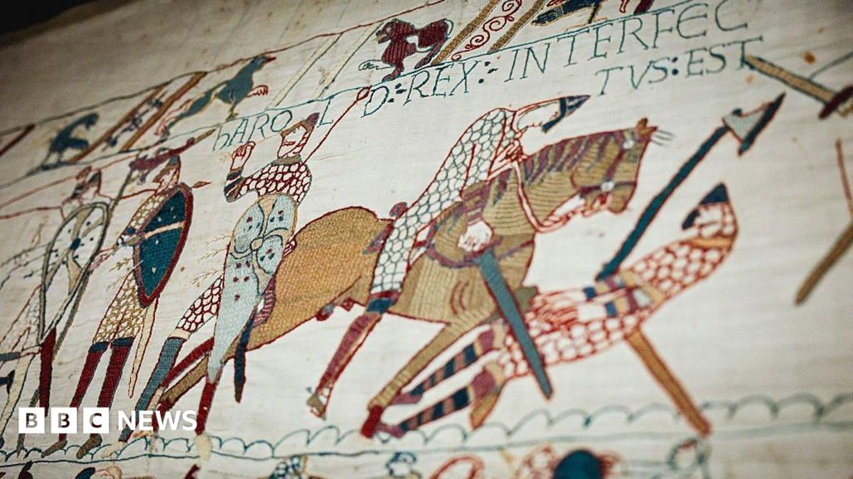 A close-up section of the Bayeux Tapestry shows embroidered figures, horses, shields and weapons in a battle scene, with decorative borders and Latin text stitched into the fabric.