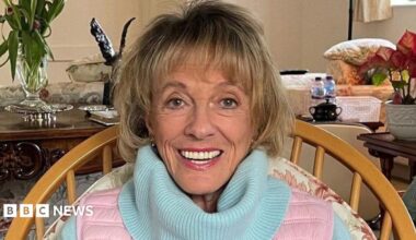 Esther Rantzen photographed towards the end of her life.  She is at home looking directly into camera and smiling.