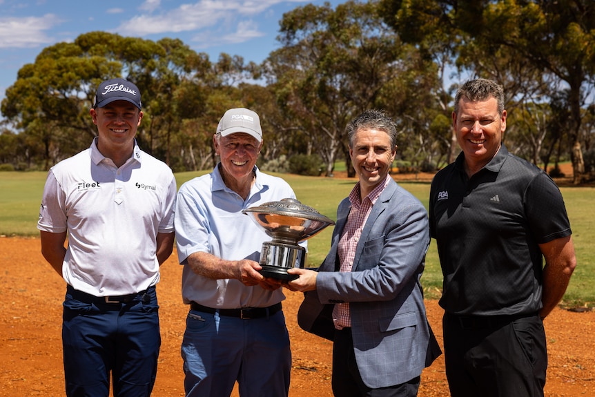 A group of four men holding a trophy at golf course.