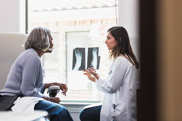 A serious female orthopedic doctor shows a senior female patient an x-ray of the patient's fractured foot. A serious female orthopedic doctor shows a senior female patient an x-ray of the patient's fractured foot.
