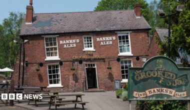 Th crooked house pub - a slanted red brick pub with a sign outside and picnic benches