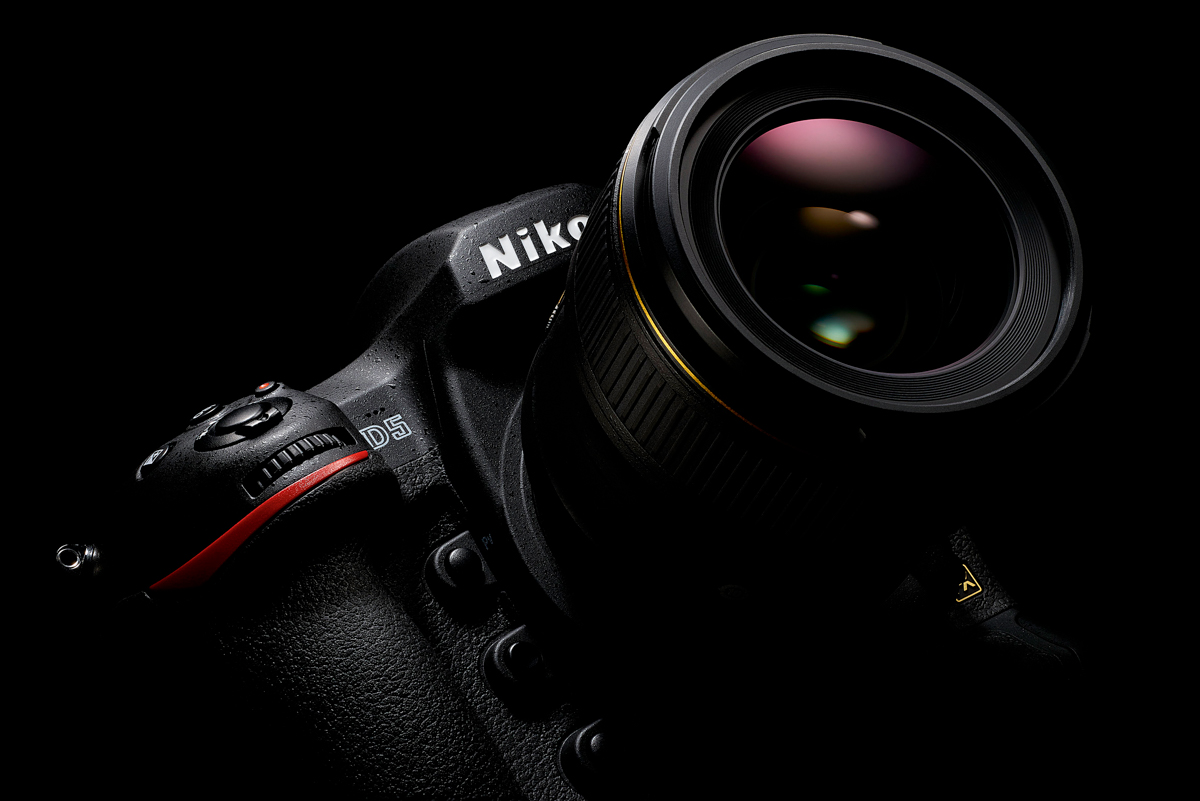 Close-up of a Nikon D5 DSLR camera with a large lens against a black background