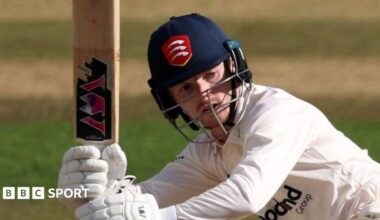 George Bell, wearing an Essex Cricket helmet, swings his bat during a match.