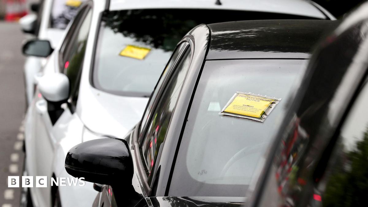 A generic-looking image shows a row of cars seen front-on with yellow and black Penalty Charge Notices affixed to their windscreens, on a road near Gatwick Airport in 2017.