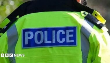 The back of  a police officer, they wear a high-vis yellow jacket that reads police on the back.