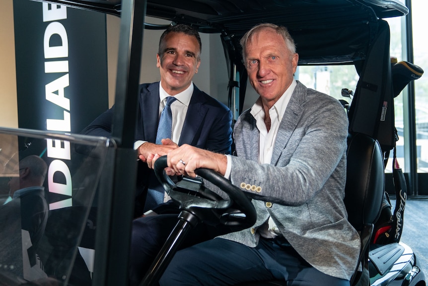 man in suit smiling next to man in sports jacket with grey hair in golf buggy
