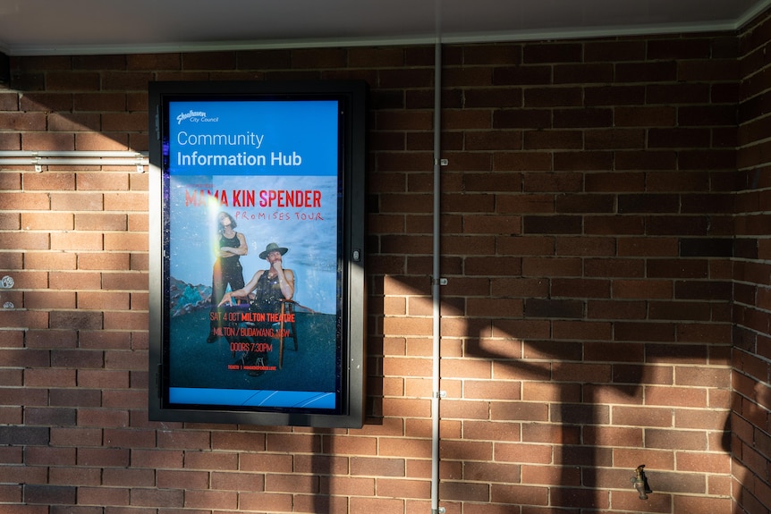 a screen attached to an exterior brick wall, with a flyer attached to it