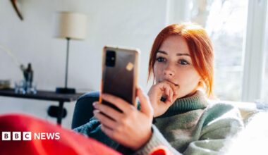 Close up of a young woman in a jumper looking at her mobile phone