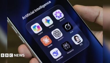 A person holds an iPhone displaying icons for Copilot, Gemini, Meta AI, Claude, ChatGPT, Grok, DeepSeek, Perplexity and Doubao in a folder titled "Artificial Intelligence"