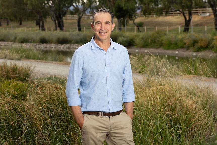 A man in a light blue shirt and brown pants standing in an outside area.